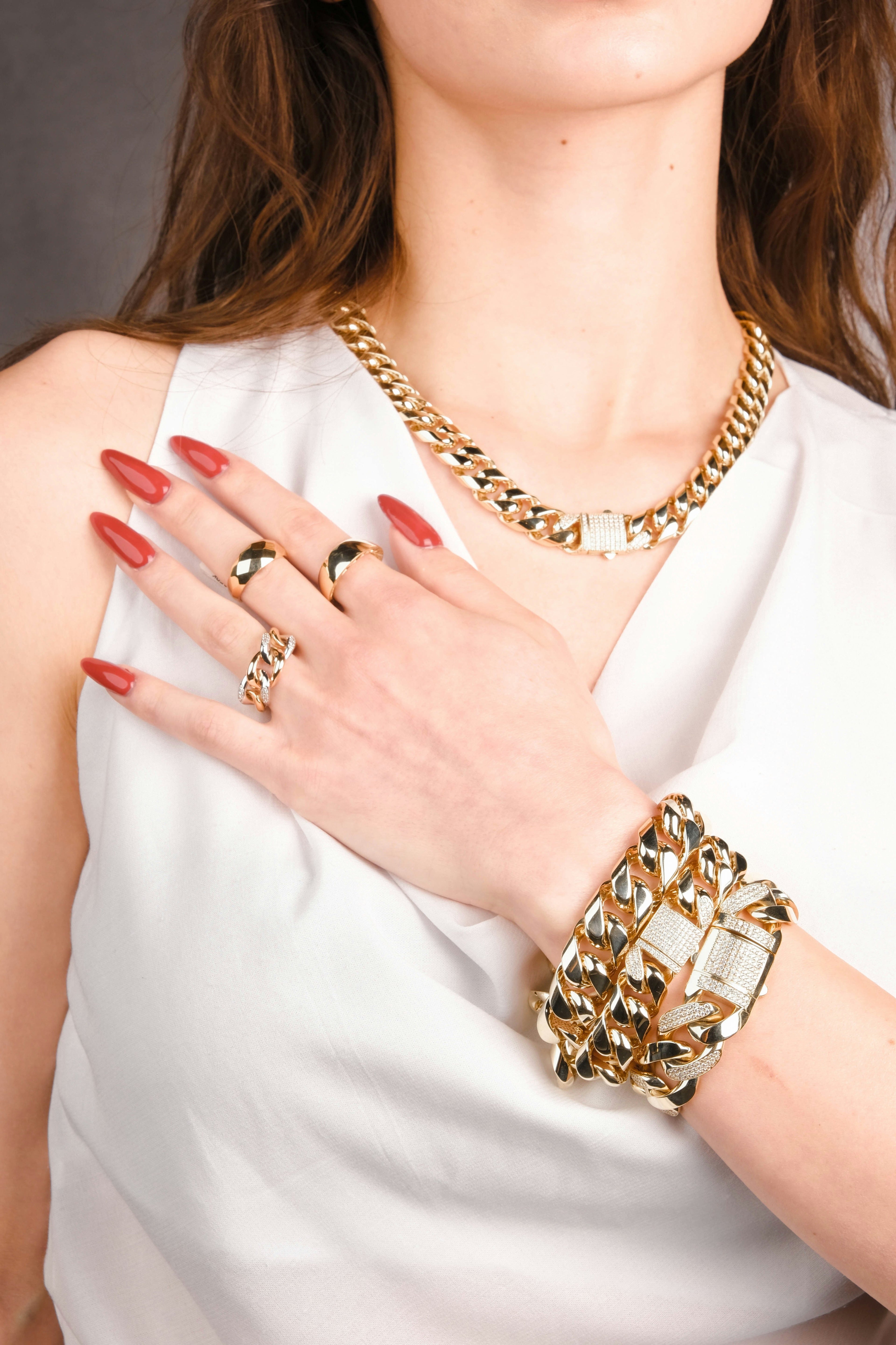 Person wearing gold jewelry including a necklace, bracelet, and rings on a plain background