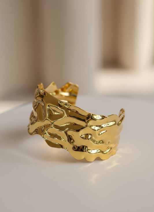 Shiny sculpted gold cuff bracelet with abstract wave pattern and polished finish.