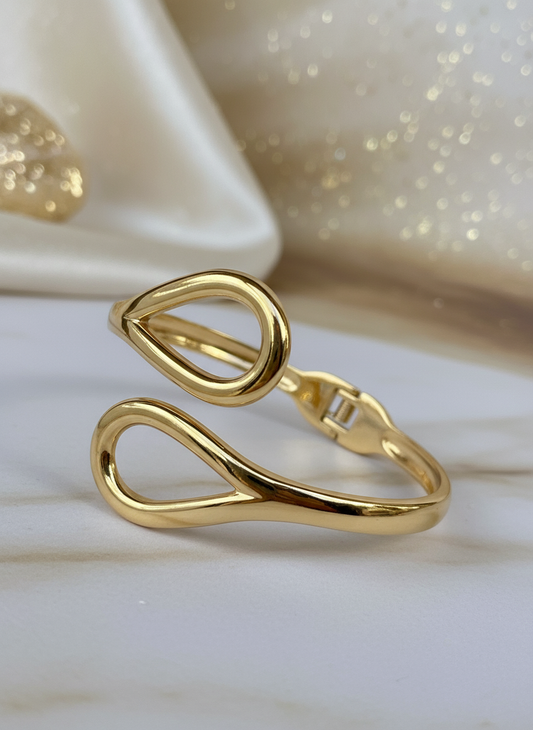 Gold open cuff bracelet with teardrop loop design on white background