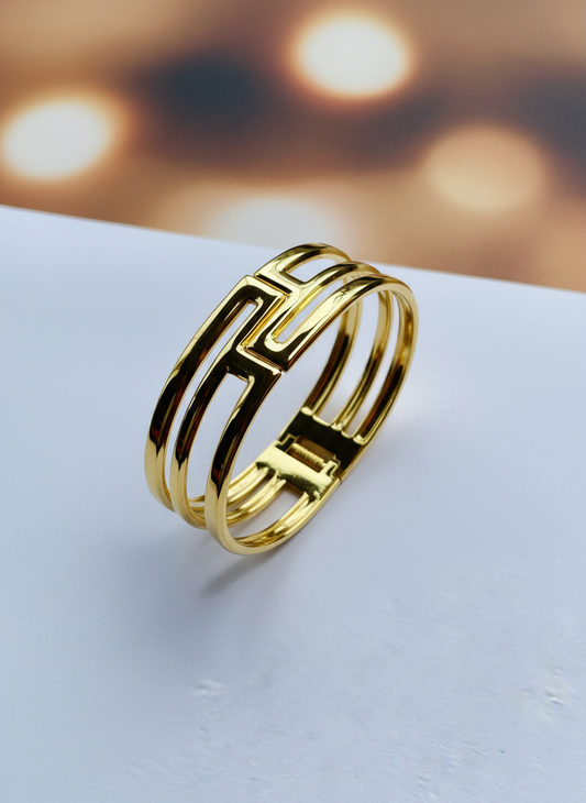 Shiny geometric gold cuff bracelet with open design and polished finish on white surface.